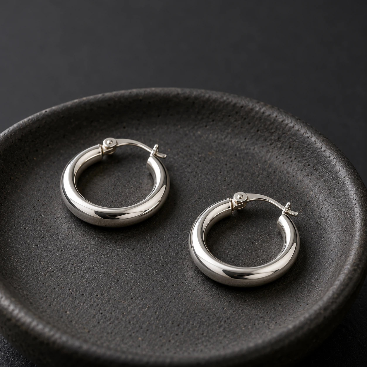 AI Black Friday product ad prompts example with two silver-tone hoops on a charcoal ceramic dish