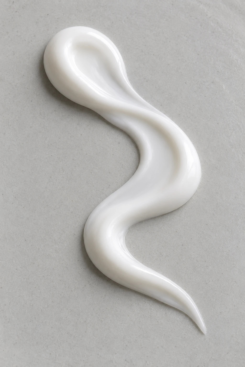 One continuous opaque lotion ribbon resting in a gentle curve on a neutral surface