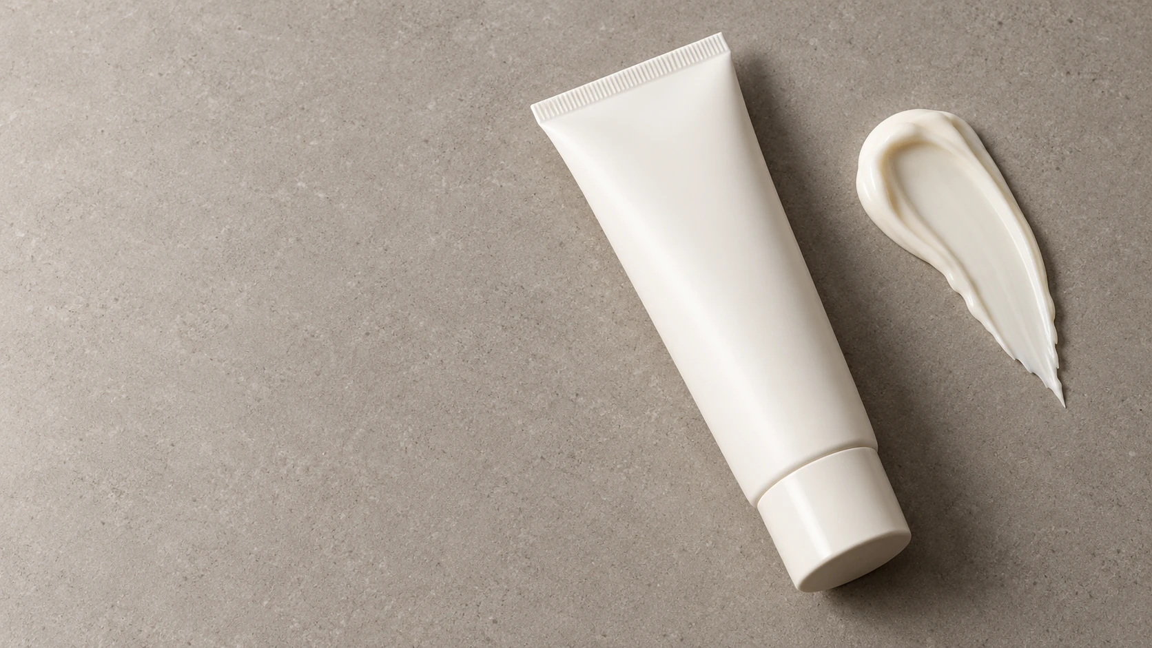 One blank skincare tube beside one separate opaque cream swatch on a plain studio surface